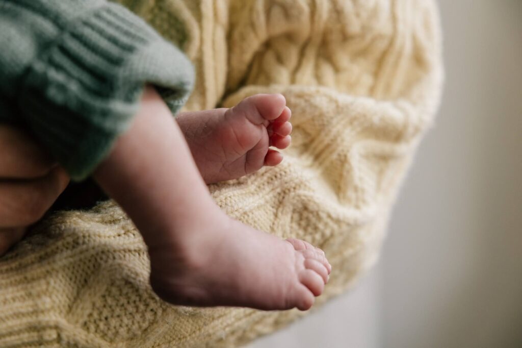 détail des pieds d’un bébé nouveau-né en tenue verte photographie naissance