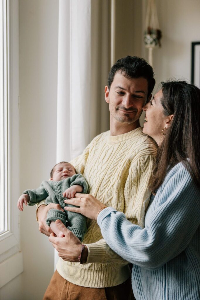 Parents tenant leur nouveau-né près d’une fenêtre pendant une séance photo naissance à Marseille 13006