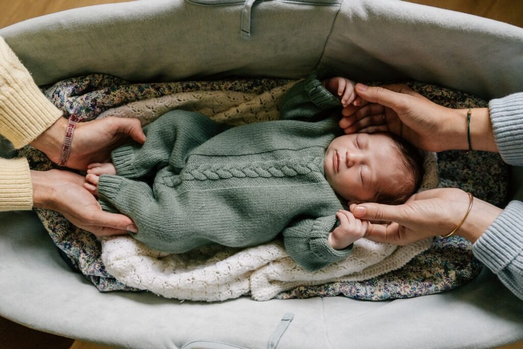 bébé nouveau-né allongé dans un couffin entouré des mains de ses parents séance photo à domicile Marseille