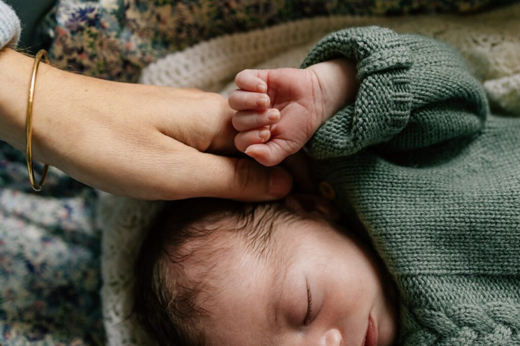 main de maman posée sur la tête de son nouveau-né pendant une séance photo bébé à domicile