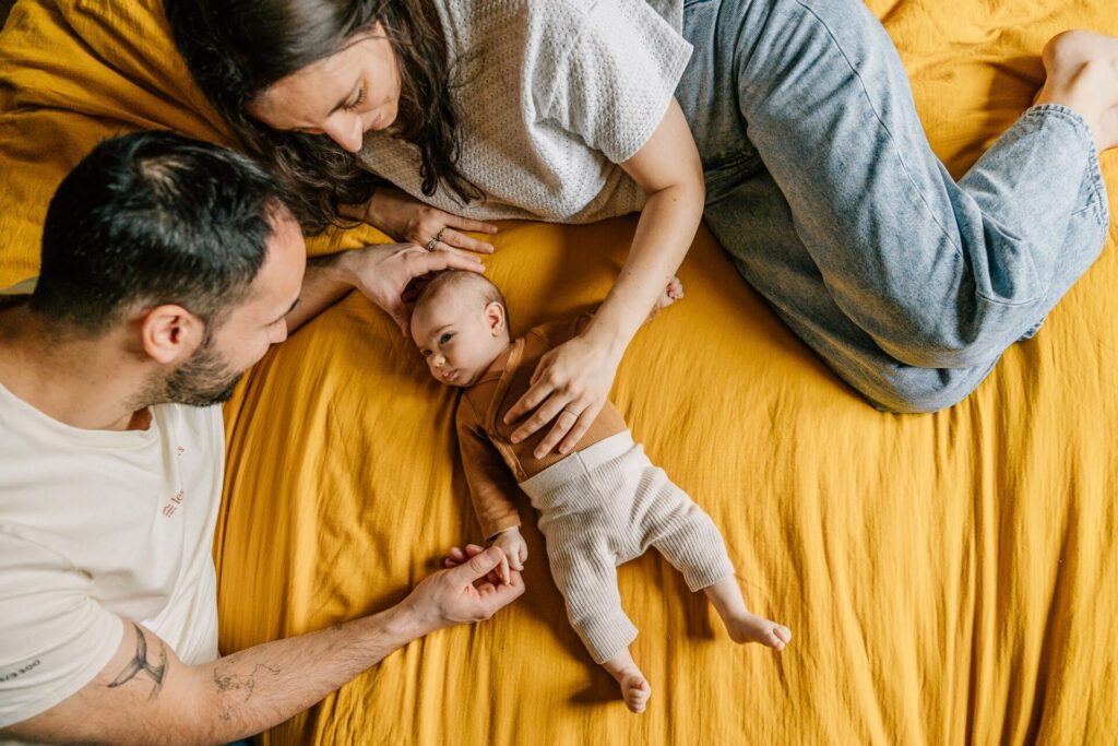 Parents allongés avec leur bébé sur un lit lors d’une séance photo famille à domicile à Marseille
