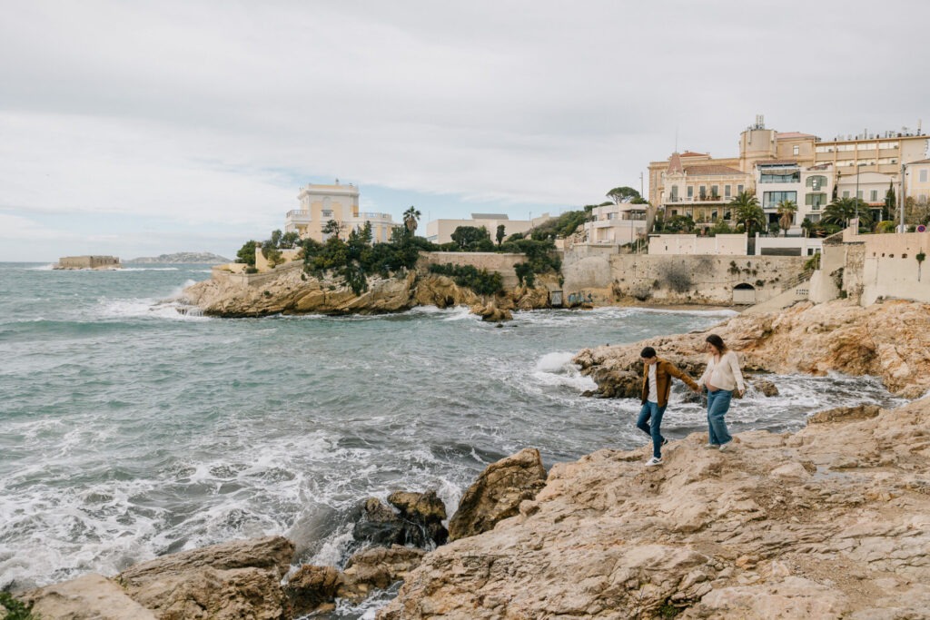 Plan large d'une photo de séance grossesse à Marseille sur les rochers de Malmousque, ambiance brute et lumière diffuse face à la Méditerranée