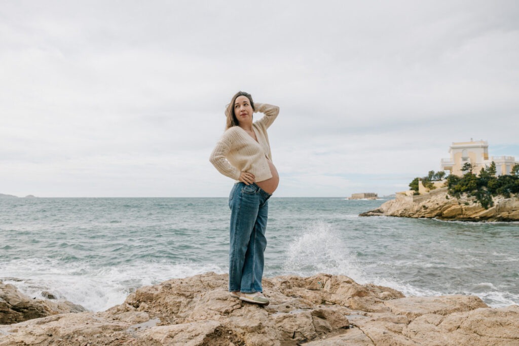Superbe portrait grossesse à Malmousque à Marseille, femme enceinte debout sur les rochers face à la mer avec les vagues agitées derrière