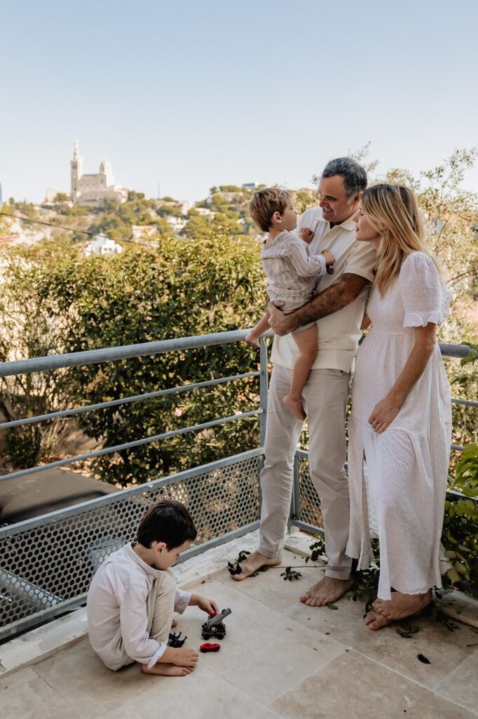 Famille sur une terrasse avec vue sur Notre-Dame de la Garde, séance photo au Roucas-Blanc à Marseille.