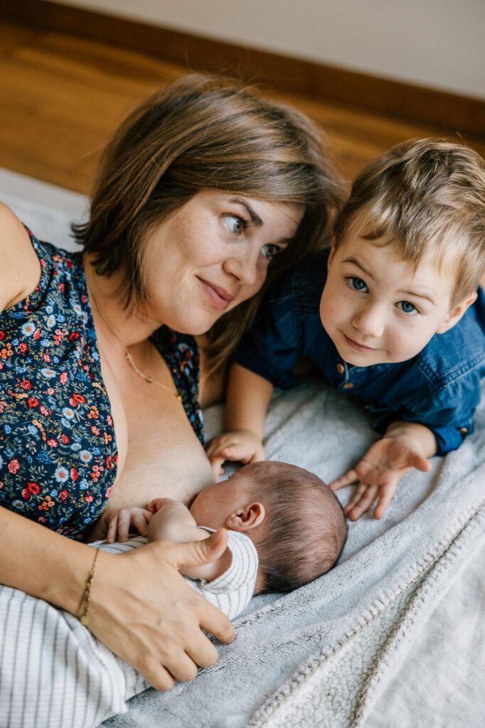 Maman et son grand garçon regardent le nouveau-né sur le lit lors d'une séance photo fratrie à domicile