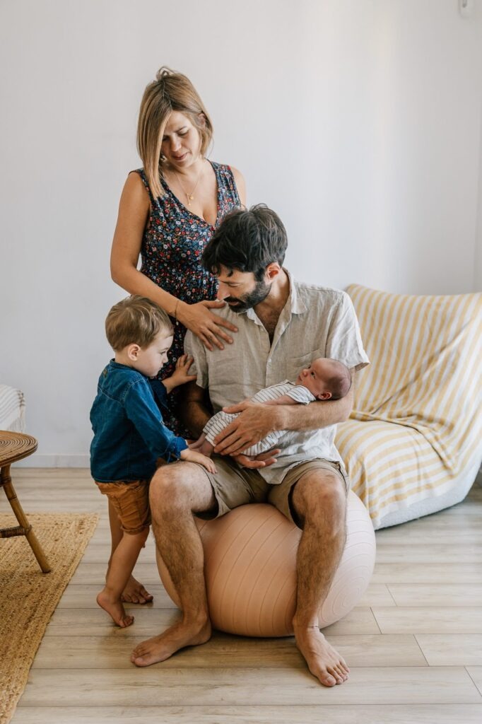 Famille réunie autour du nouveau-né dans le salon lors d'une séance photo à domicile