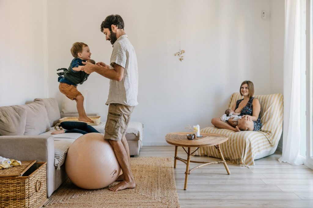 Séance photo nouveau-né à domicile à L'Estaque, Marseille : papa joue avec le grand frère pendant que maman tient le bébé