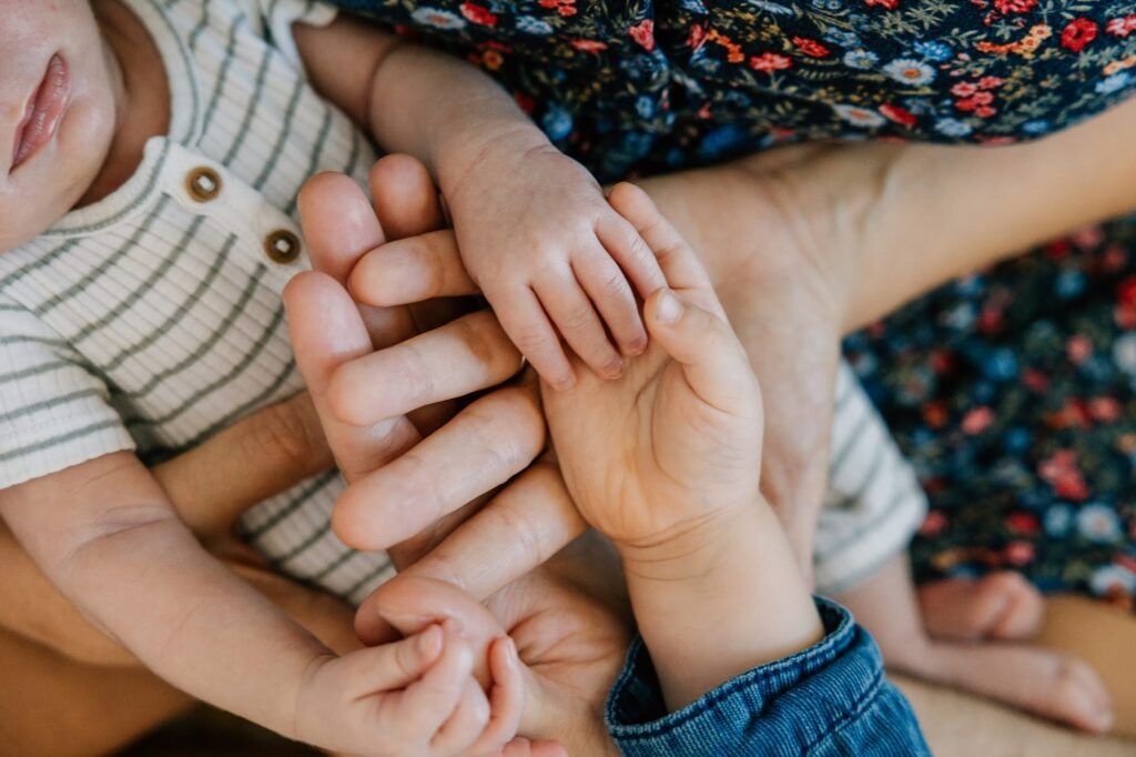 Détail des mains du grand frère et du nouveau-né, premier contact entre la fratrie