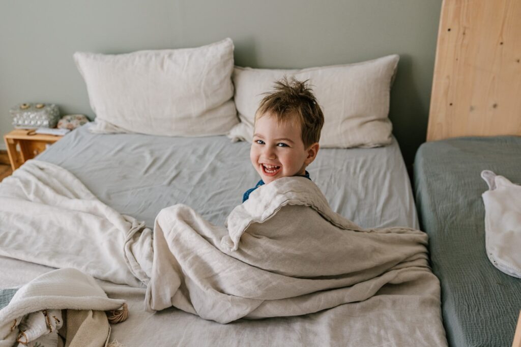 Portrait naturel du grand frère souriant sur son lit lors d'une séance photo à domicile