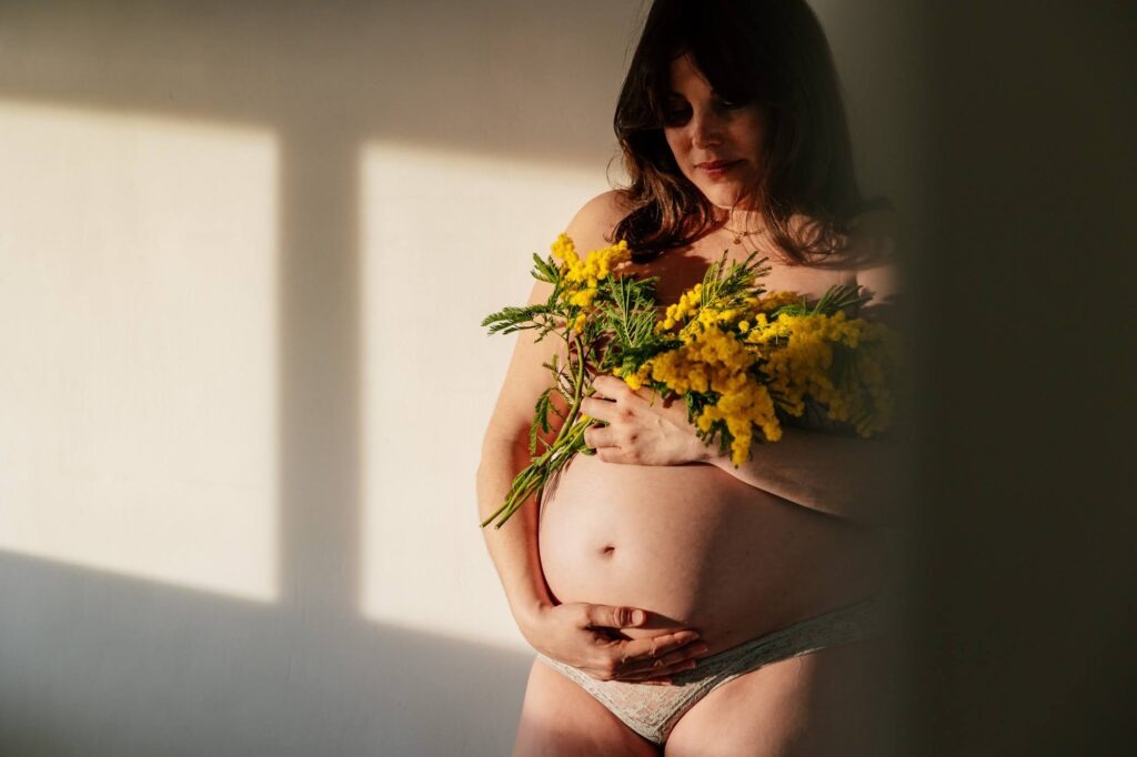 Femme enceinte tenant un bouquet de mimosa lors d'une séance photo de grossesse à domicile à Marseille