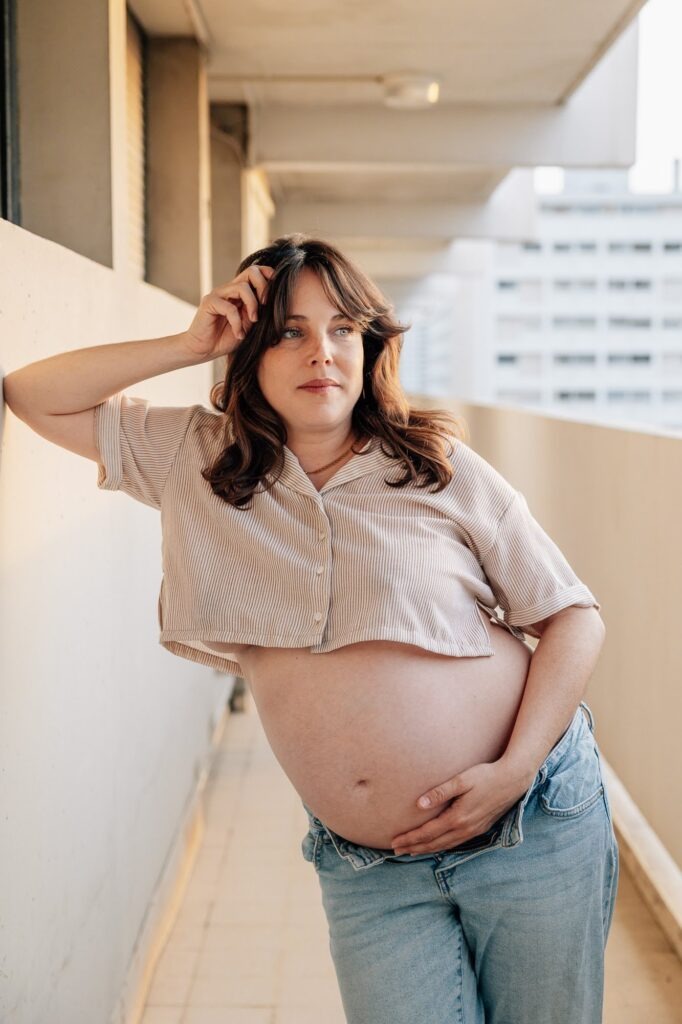 Femme enceinte en jean sur un balcon lors d'une séance photo de grossesse à Marseille