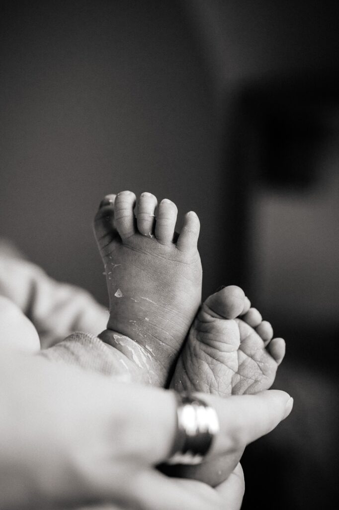 Détail des pieds d’un bébé nouveau-né dans les mains d’un parent pendant une séance photo naissance