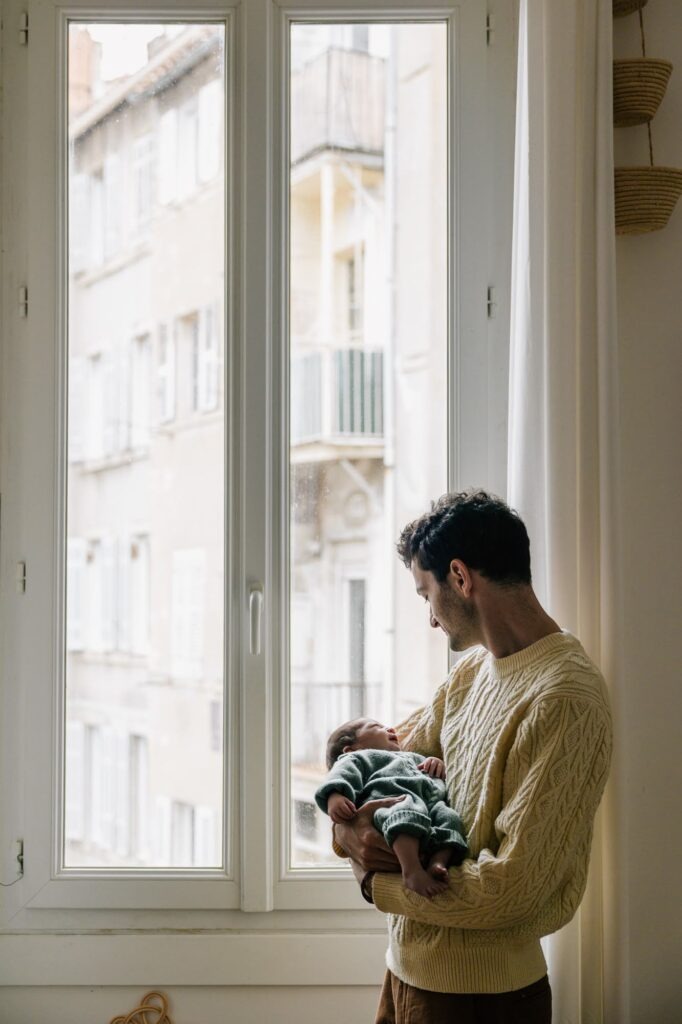 papa tenant son bébé près de la fenêtre lumière naturelle séance photo naissance