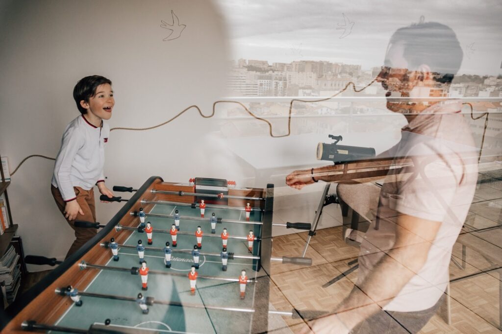 Père et fils au babyfoot, reflet dans la vitre, séance photo famille à domicile Marseille